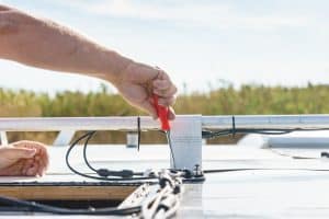 A close-up of a person using a screwdriver to tighten a bracket for a solar panel on the roof of a recreational vehicle.